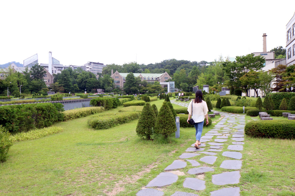 Ewha University student walking on stone path through green campus area